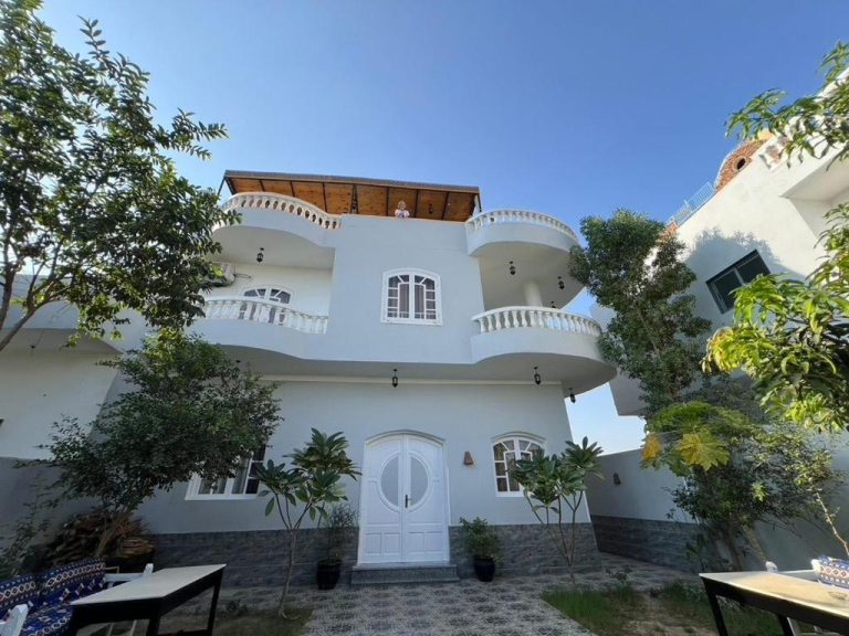 Fachada exterior blanca del Panorama Hotel con balcones curvos y jardín tropical de tres plantas