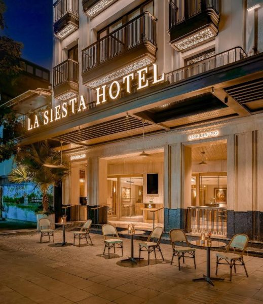 Fachada exterior iluminada del La Siesta Premium Lakeside Hotel con terraza y mesas en la entrada
