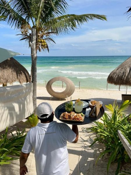 Mesero sirviendo tacos y margaritas frente a la playa del Hotel Sueños Tulum con vista al mar Caribe