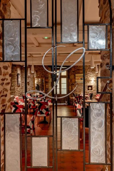 Entrada decorativa de forja con cristal y monograma del Hotel Restaurant Lesage con comedor interior