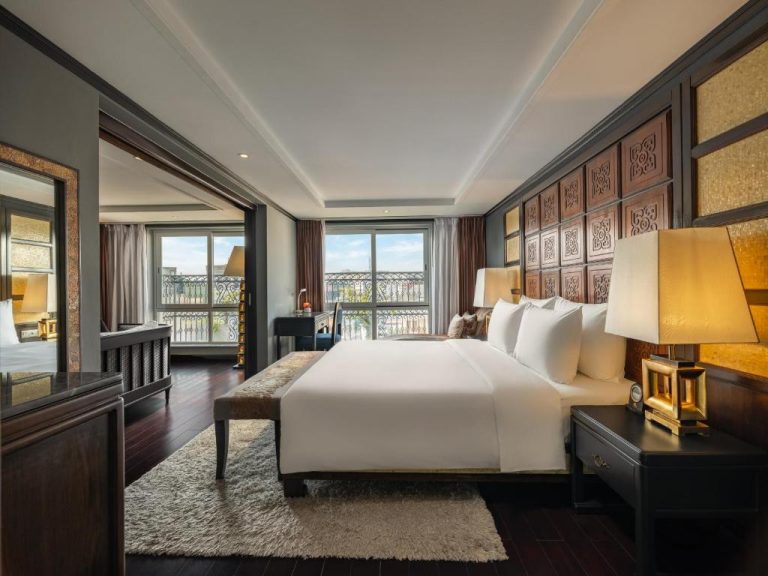 Suite de lujo con cama king, cabecero de madera tallada y balcón con vistas en Hanoi Solis Hotel