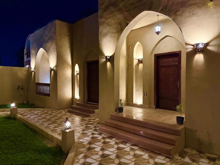 Entrada exterior iluminada del Bab Al Shams Palace con arcos árabes y jardín por la noche