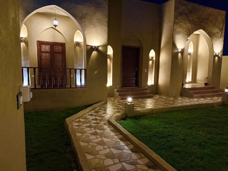 Jardín exterior iluminado con arcos árabes y camino de piedra del Bab Al Shams Palace de noche