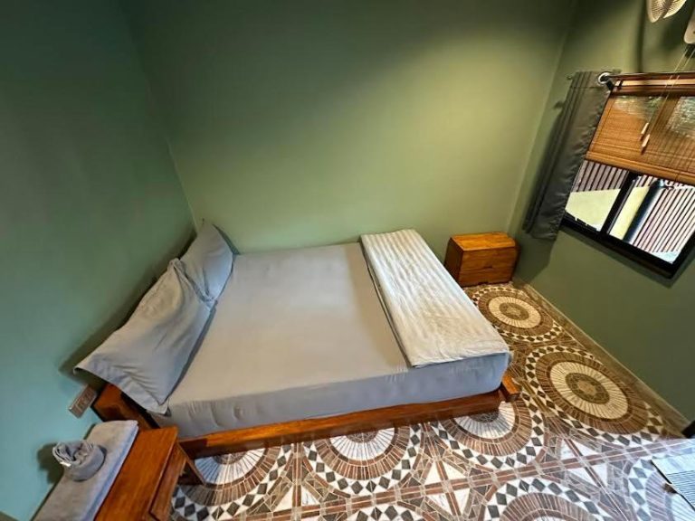 Habitación doble con cama de madera, paredes verdes y suelo hidráulico en Soul of Lanta