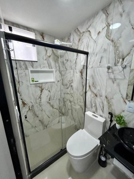 Banheiro moderno com revestimento de mármore e box de vidro na Pousada Ilha da Fantasia