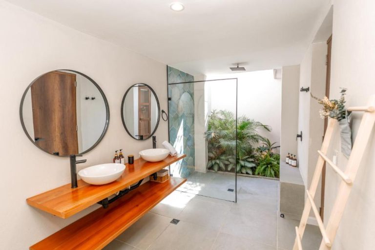 Baño doble con lavabos sobre encimera de madera y ducha con jardín tropical en Hotel Libreria Cafe de Pombal
