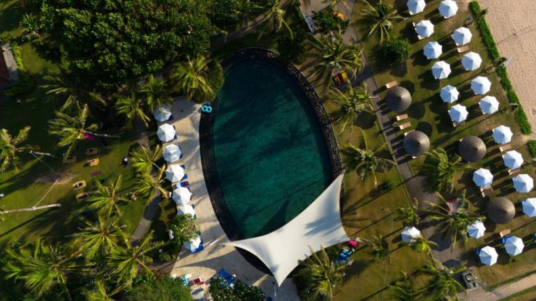 Vista aérea de la piscina principal rodeada de palmeras y sombrillas del Ayodya Resort Bali
