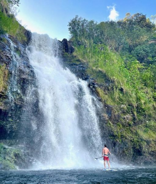 Huésped en paddleboard frente a la impresionante cascada natural de The Inn at Kulaniapia Falls en Hawaii