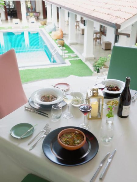 Mesa con platos gourmet y vino en el restaurante terraza con vistas a la piscina de La Maison de Colombo