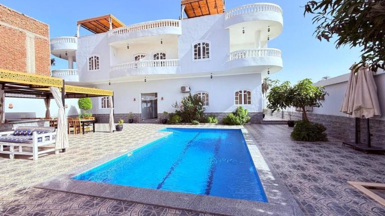 Piscina exterior azul con terraza y jardín del Panorama Hotel frente a villa blanca de varios pisos