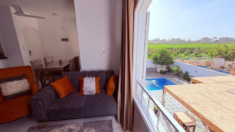 Salón con sofá gris y vistas a la piscina exterior del Panorama Hotel rodeado de vegetación