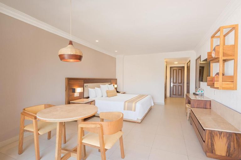Habitación Junior Suite con cama doble, mesa de comedor y decoración en madera del Royal Solaris Los Cabos