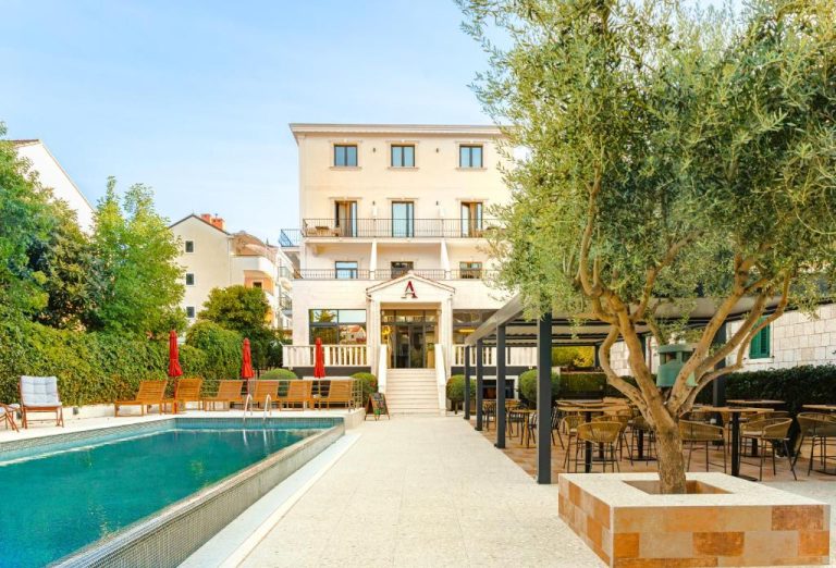 Piscina exterior y terraza con mesas del Hotel Aquarius Dubrovnik rodeada de olivos y tumbonas