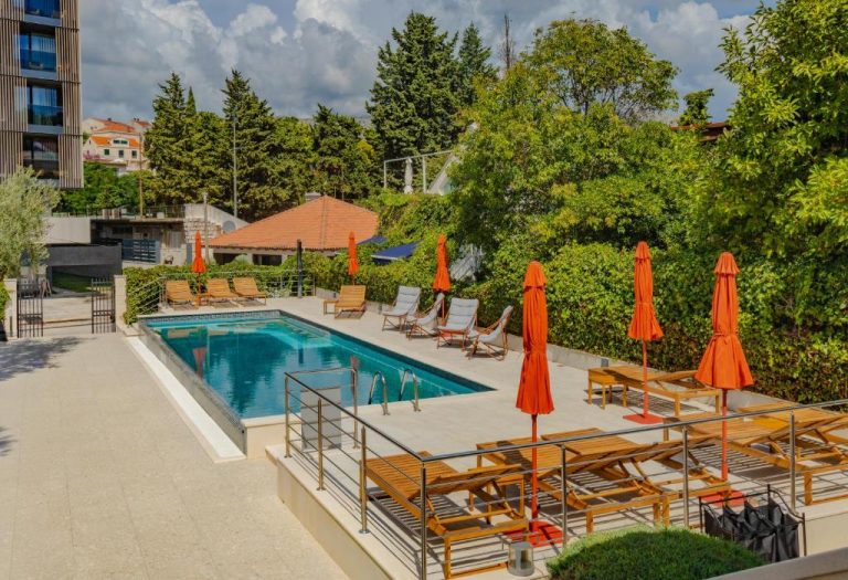 Piscina exterior con tumbonas y sombrillas naranja del Hotel Aquarius Dubrovnik rodeada de vegetación