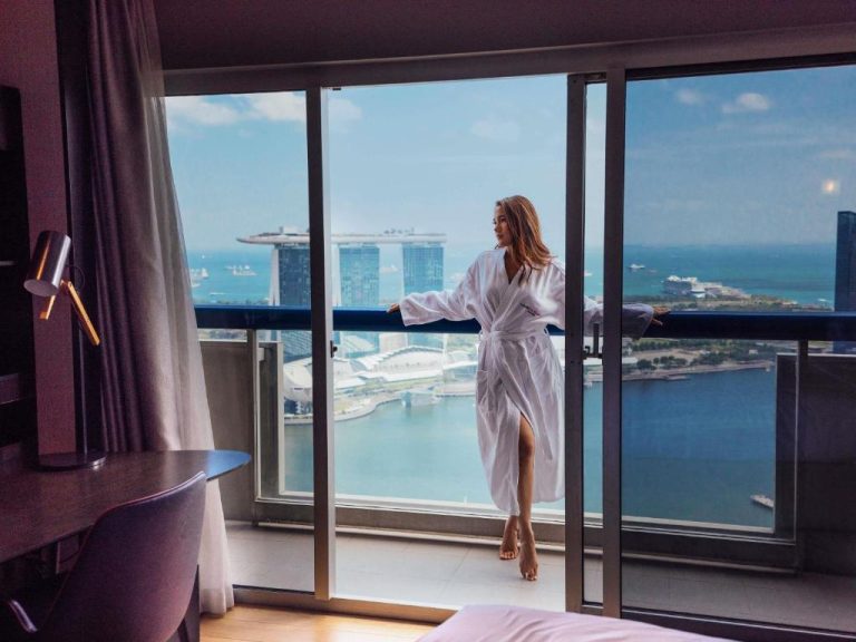 Mujer en bata blanca en balcón del Swissotel The Stamford Singapore con vistas a Marina Bay Sands