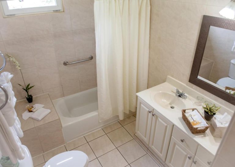 Baño completo con bañera y ducha del Aruba Surfside Marina, decorado en tonos blancos y beige