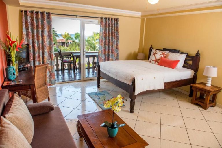 Habitación doble con cama de madera, balcón con vistas tropicales y salón en Aruba Surfside Marina