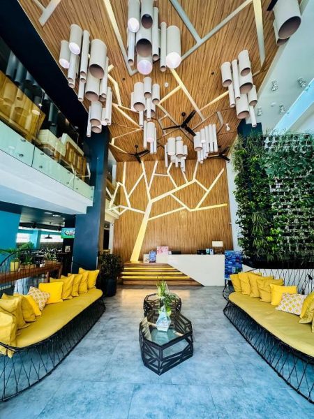 Lobby moderno del Ferra Hotel and Garden Suites con sofás amarillos, jardín vertical y árbol decorativo iluminado