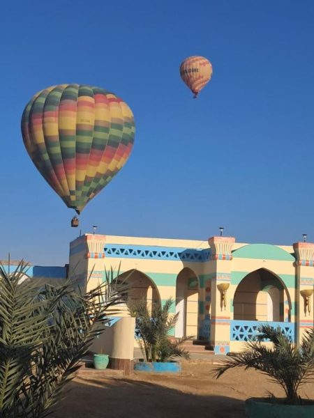 Globos aerostáticos sobrevolando la fachada del Aton Palace Luxor con palmeras y cielo azul
