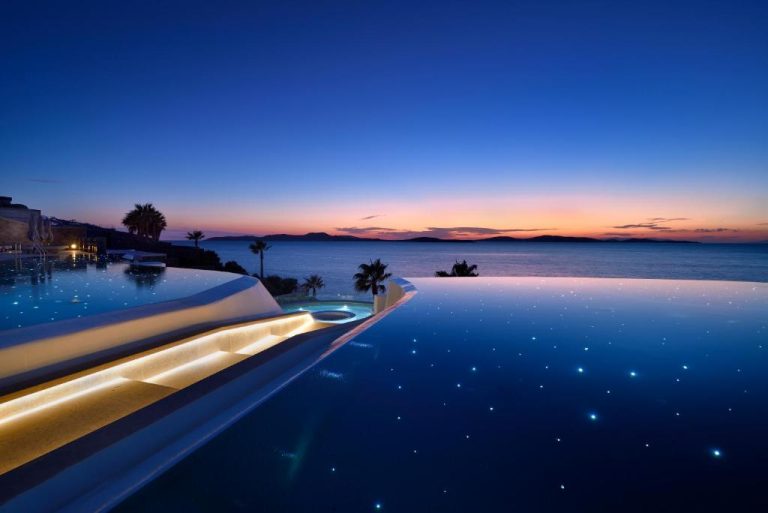 Piscina infinita iluminada al atardecer con vistas al mar en Anax Resort and Spa Mykonos