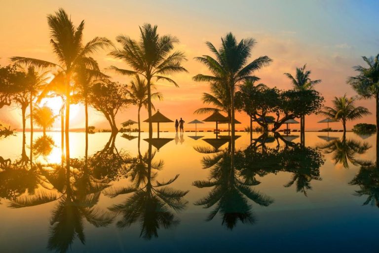 Piscina infinita con palmeras reflejadas al atardecer en el Ayodya Resort Bali