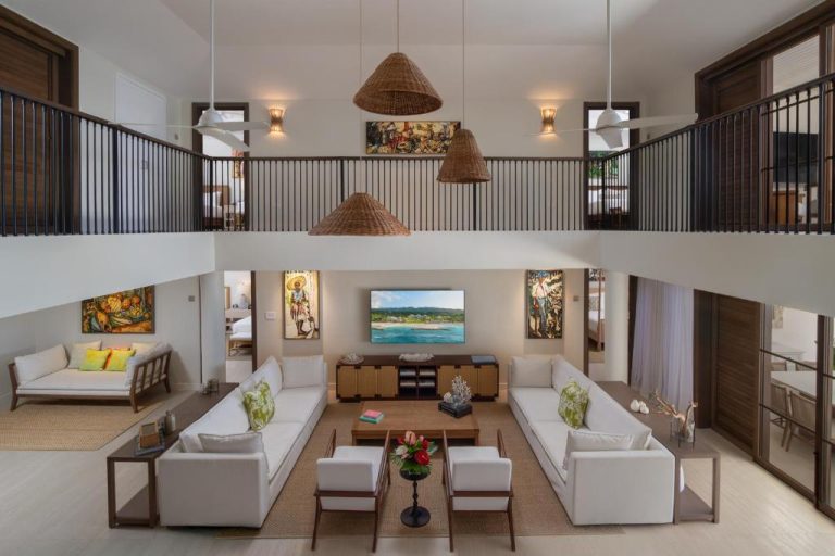 Amplio salón de doble altura con sofás blancos, arte caribeño y balcón interior en Half Moon Resort