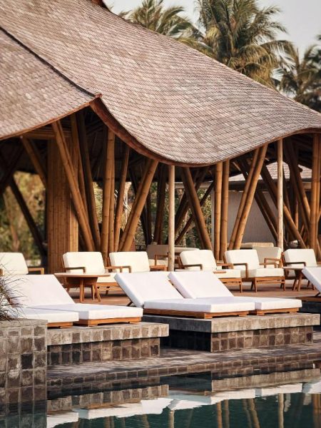 Zona de solarium con tumbonas blancas junto a la piscina bajo estructura de bambú en RAH GILI Maldives