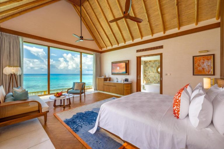 Habitación overwater con cama king y vistas al océano turquesa en RAH GILI Maldives