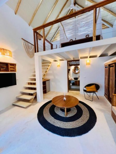 Salón con altillo y escaleras del Leeloo Boutique Hotel, decoración rústica tropical con mesa de madera
