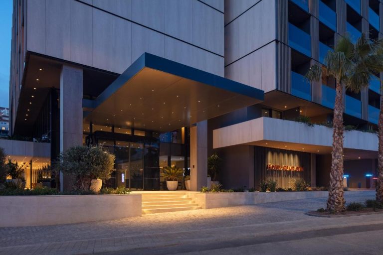 Entrada principal iluminada del Hotel Sumratin con palmeras y escalinatas modernas al atardecer