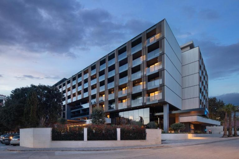Fachada exterior moderna del Hotel Sumratin al atardecer con iluminación interior y jardines