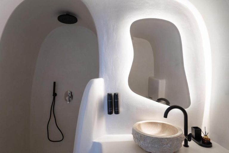 Baño de cueva con lavabo de piedra natural y ducha empotrada en You and Me Suites Oia