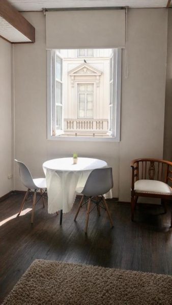 Habitación con mesa y sillas blancas frente a ventana con vistas al edificio histórico en el centro de la ciudad