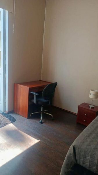 Habitación con escritorio de madera, silla de oficina y mesita de noche con lámpara con vista al corazón de la ciudad