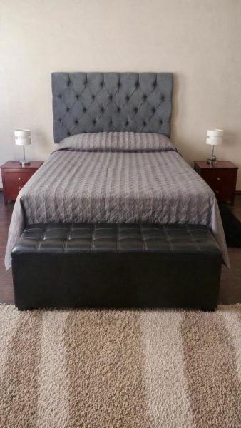 Habitación doble con cama tapizada en gris, mesitas de noche y banco de cuero negro con vista al centro de la ciudad