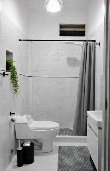 Baño moderno con ducha y revestimiento de mármol blanco en habitación con balcón vista ciudad