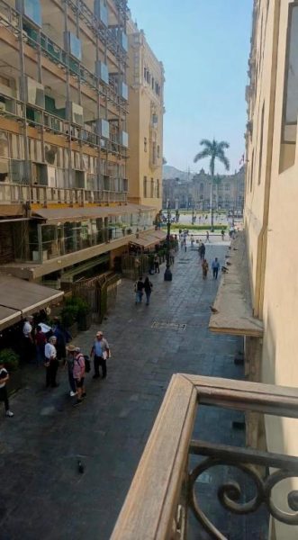 Vista desde el balcón de la habitación hacia la Plaza Mayor de Lima con transeúntes y palmeras