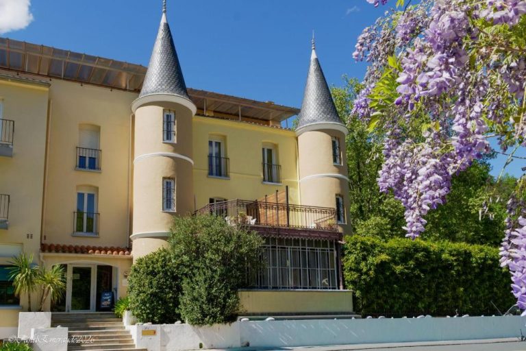 Fachada exterior del Appart'Hotel Castel Emeraude con torres y glicinas en flor