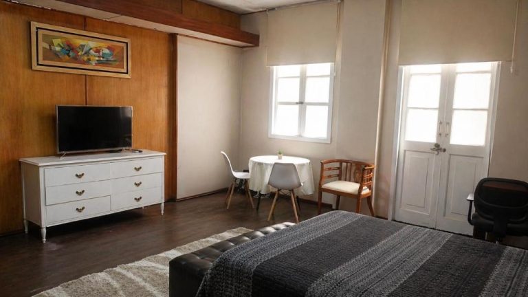 Habitación con balcón y vista a la ciudad, cama doble, televisor y zona de comedor interior