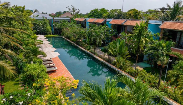 Piscina exterior rodeada de jardín tropical en el Khmer House Resort con tumbonas y bungalows