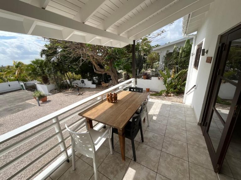 Terraza exterior con mesa de madera y sillas en Bantopa Apartments, rodeada de jardín tropical