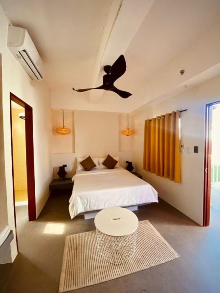 Habitación doble con cama matrimonial, ventilador de techo y cortinas amarillas en Happiness Hostel Boracay
