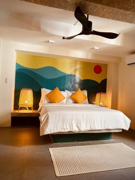 Habitación doble con mural de montañas y sol en Happiness Hostel Boracay, cama king y lámparas de bambú