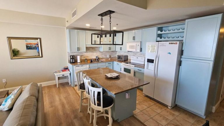Cocina moderna con isla de granito y gabinetes azules en Gulf View Condo con acceso directo a la playa