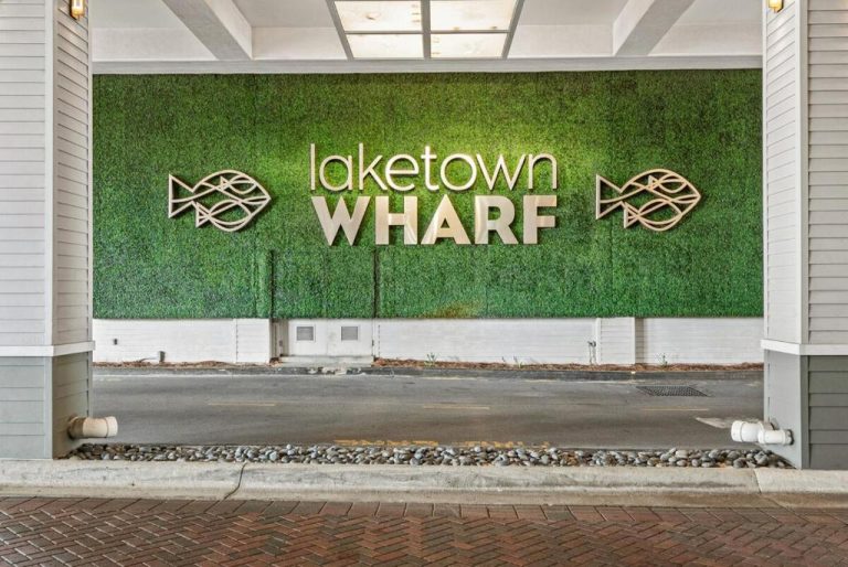 Entrada principal de Laketown Wharf con muro vegetal verde y letrero decorativo con peces