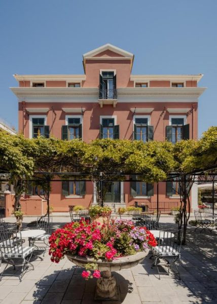 Fachada neoclásica rosa del Hotel Bella Venezia con terraza exterior y jardín con flores