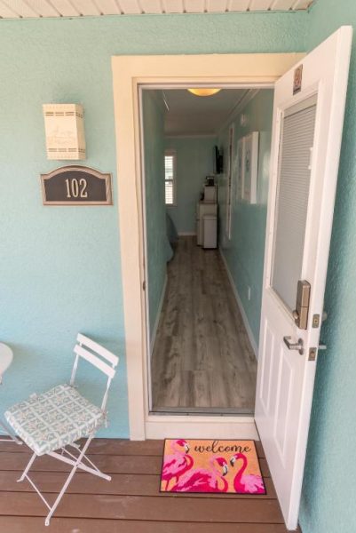 Entrada de la habitación 102 del Flamingo Inn con felpudo de bienvenida y decoración tropical en tonos turquesa