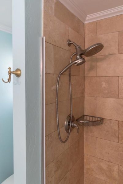 Ducha con alcachofa extensible y estante metálico en baño con azulejos del Flamingo Inn