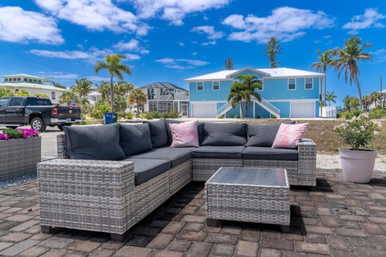 Terraza exterior con sofá de ratán gris y cojines rosas del Flamingo Inn con palmeras al fondo