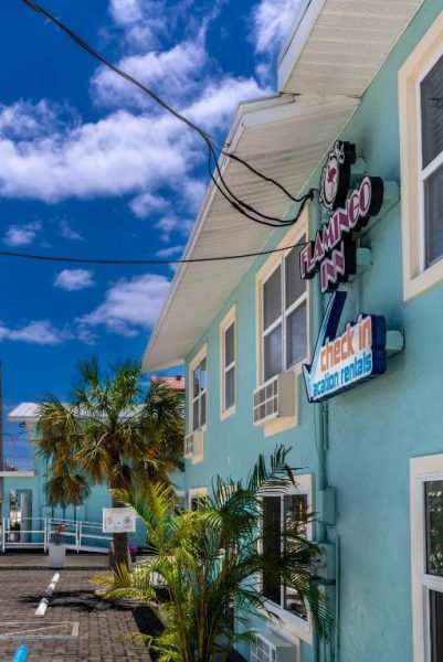 Fachada exterior del Flamingo Inn con cartel de check-in y alquileres vacacionales rodeado de palmeras